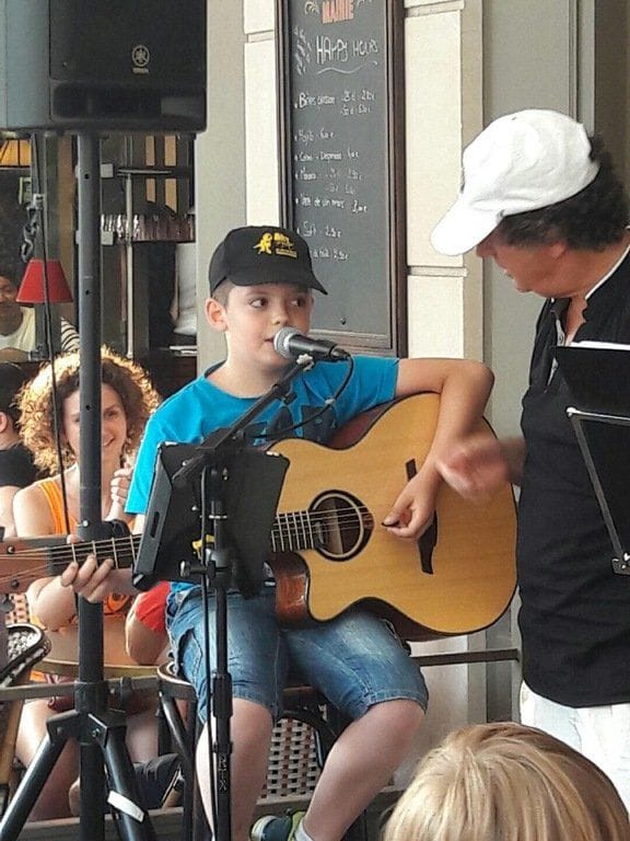 Un jeune élève chante au micro en s’accompagnant à la guitare acoustique.