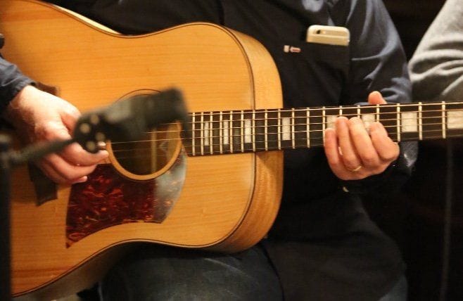 Gros plan sur les mains d’un guitariste jouant d’une guitare acoustique.